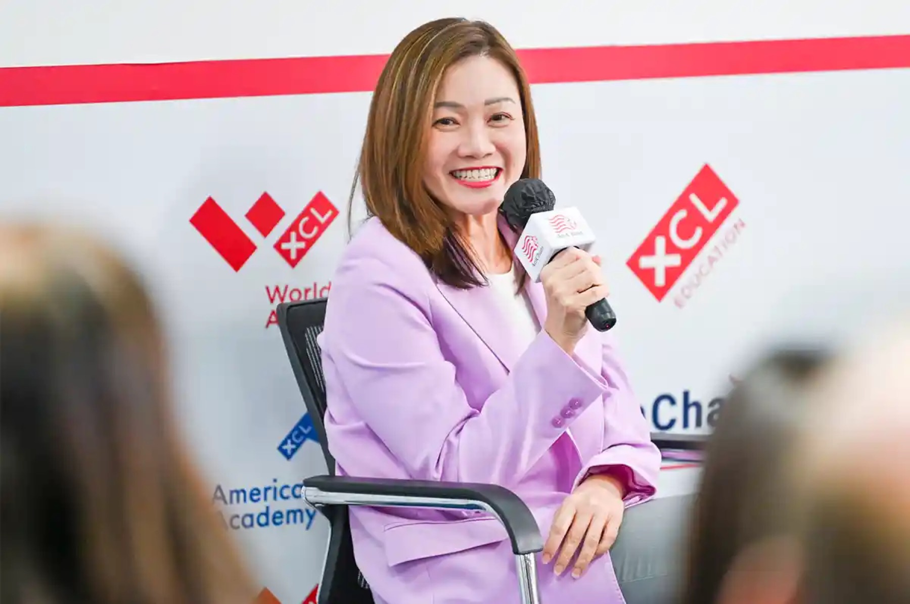 A speaker with a microphone smiling on stage at an AmCham Singapore session